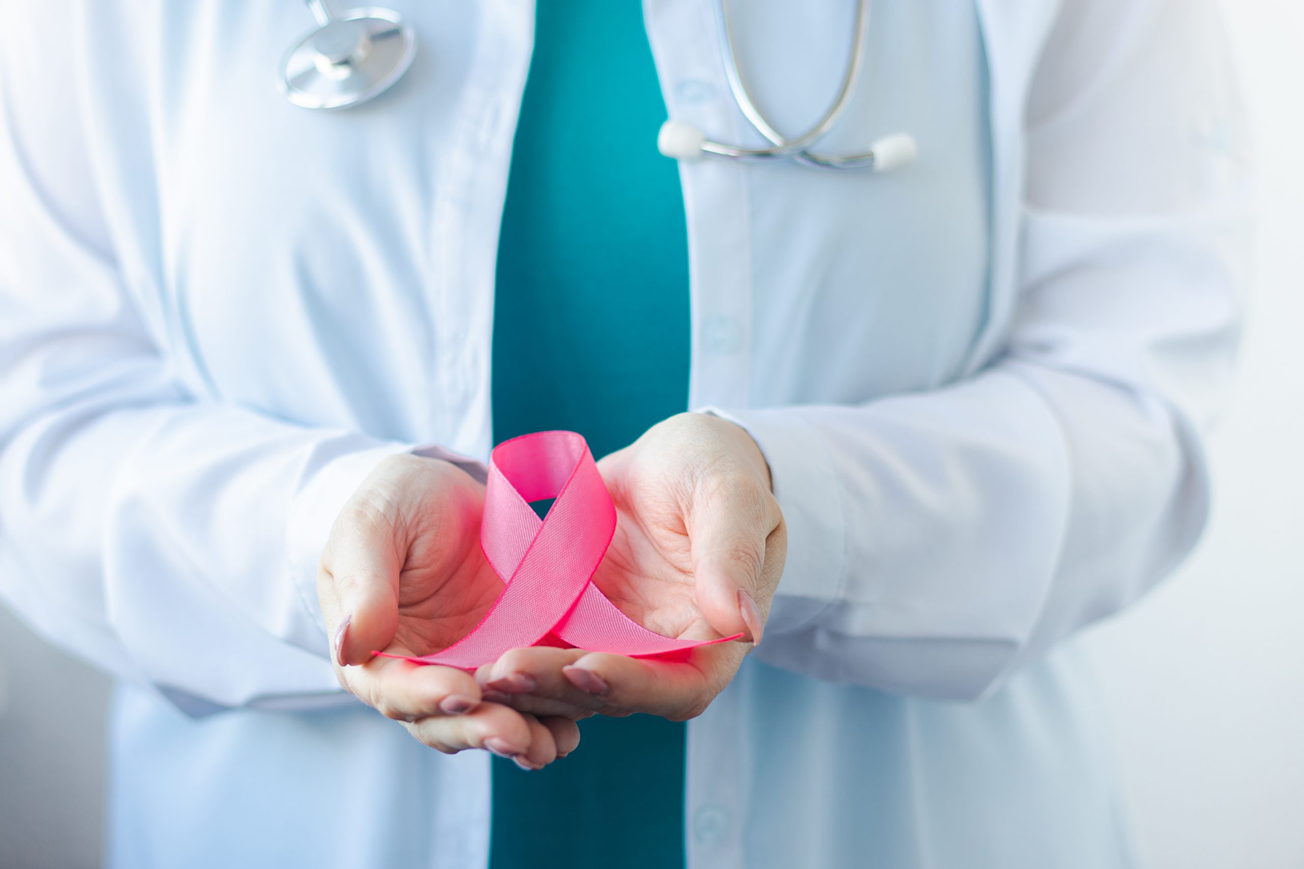 Breast Cancer Awareness Month. Female doctor in medical white uniform holds pink ribbon in her hands. Women's health care concept.