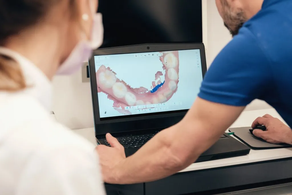 Anonymous male dentist demonstrating teeth scan on laptop screen to unrecognizable woman dentist in modern clinic